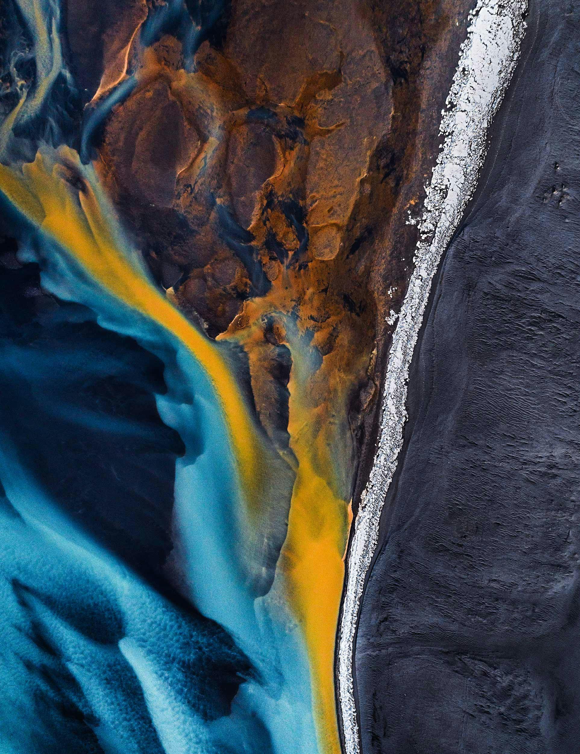 Aerial shot looking down on a braided river at the edge of a black sand beach, Iceland.